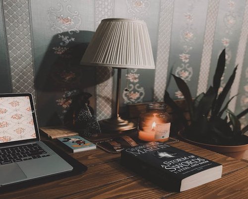 A cozy reading nook with a warm desk lamp and a closed laptop on a wooden table